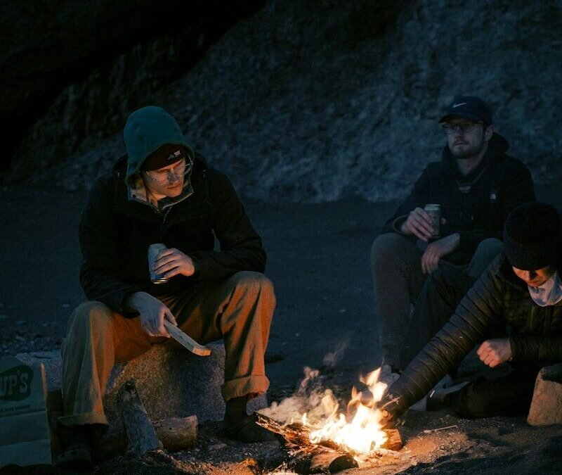 man sitting on brown log near bonfire during daytime